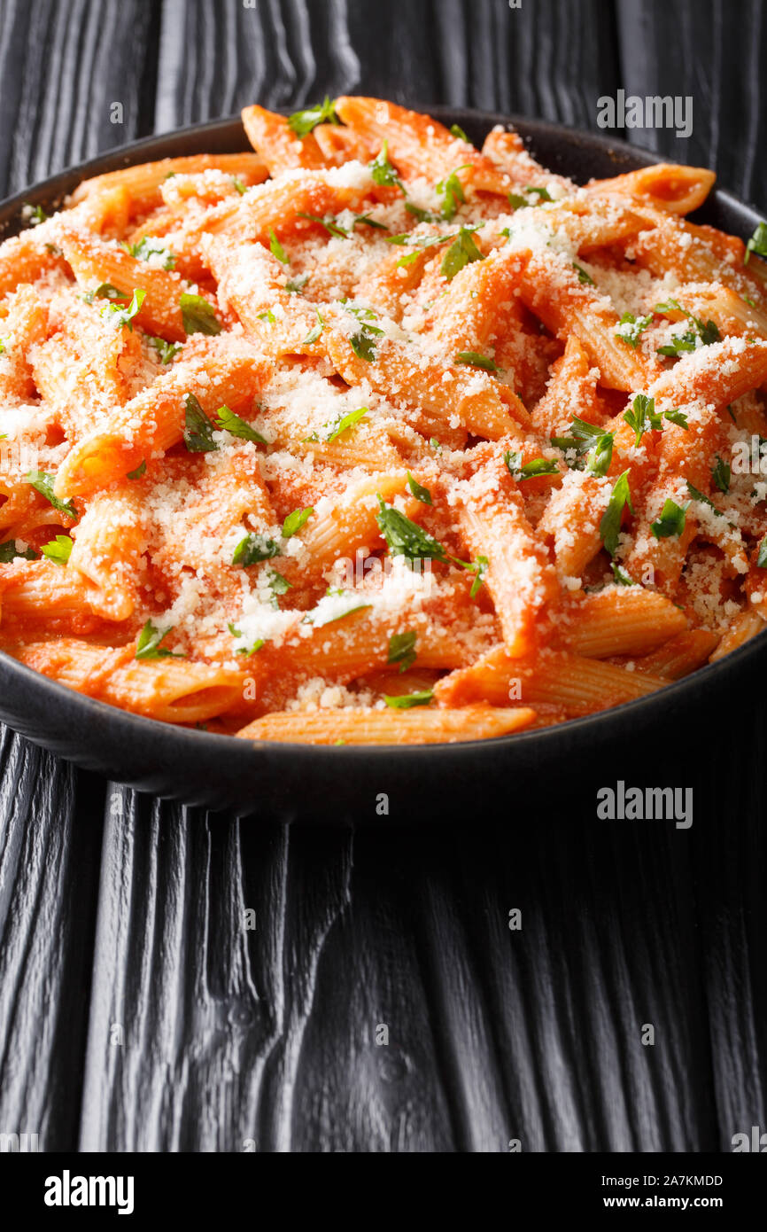 Italian penne pasta alla vodka topped with parmesan and parsley closeup in a plate on the table