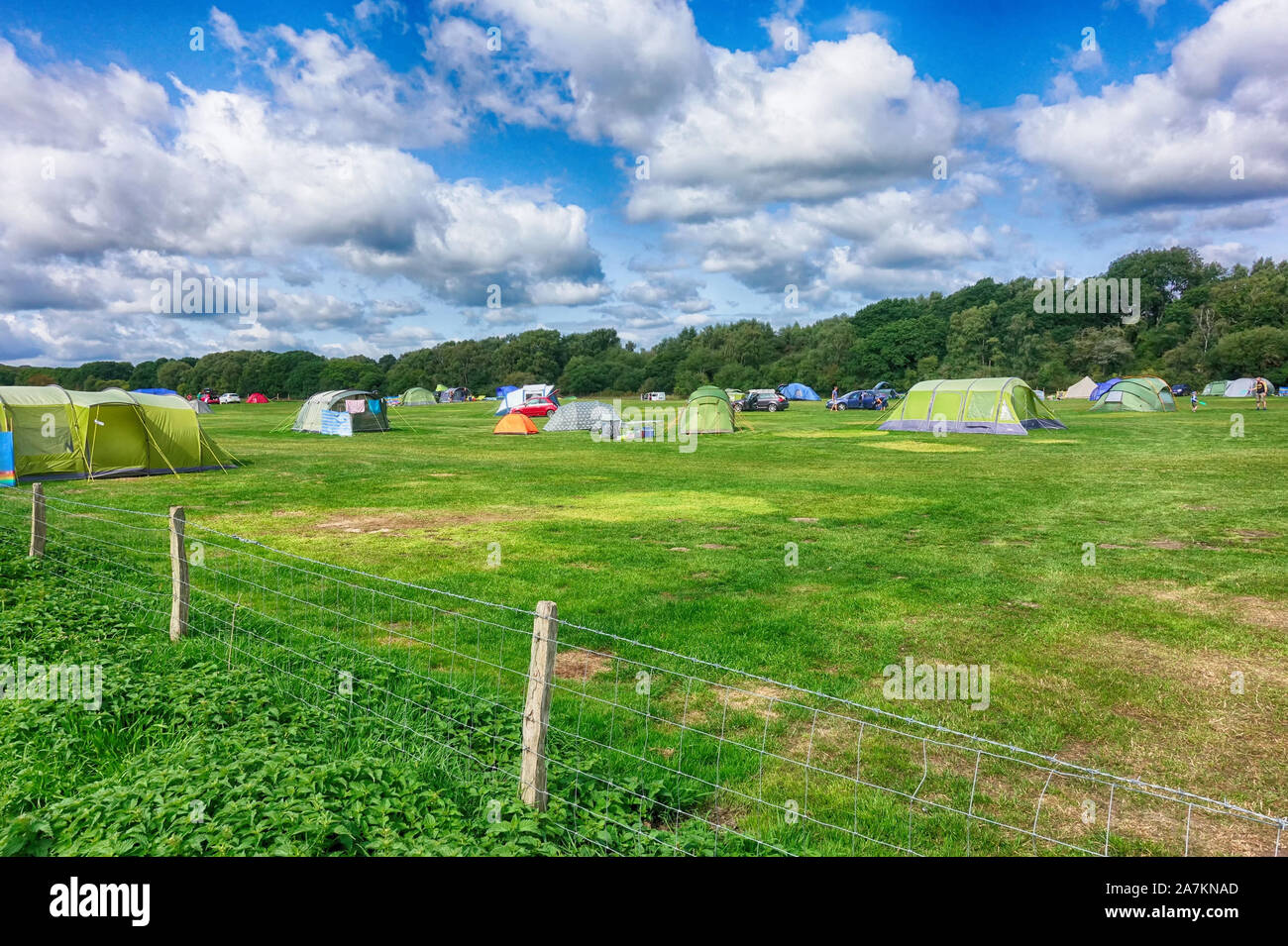 Norden, England - Aug 29 2018: Colorful tents on a green field campsite under blue cloudy sky, with people camping and putting up their tent Stock Photo