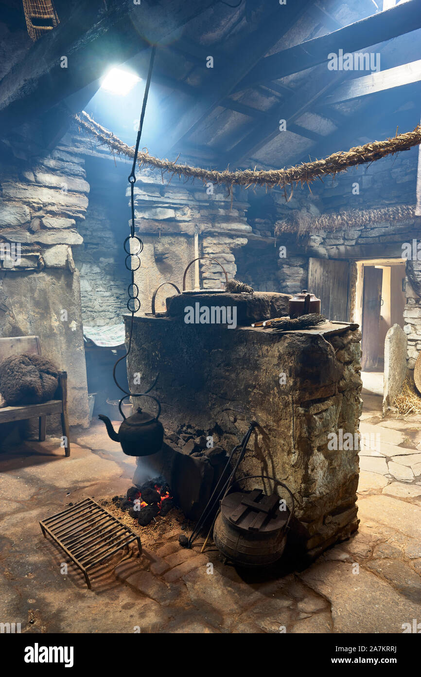 Interior of the Kirbuster Farm Museum, a firehoose, showing the central stone hearth, peat fire and hanging kettle, Kirbuster, Mainland, Orkney, Scotl Stock Photo
