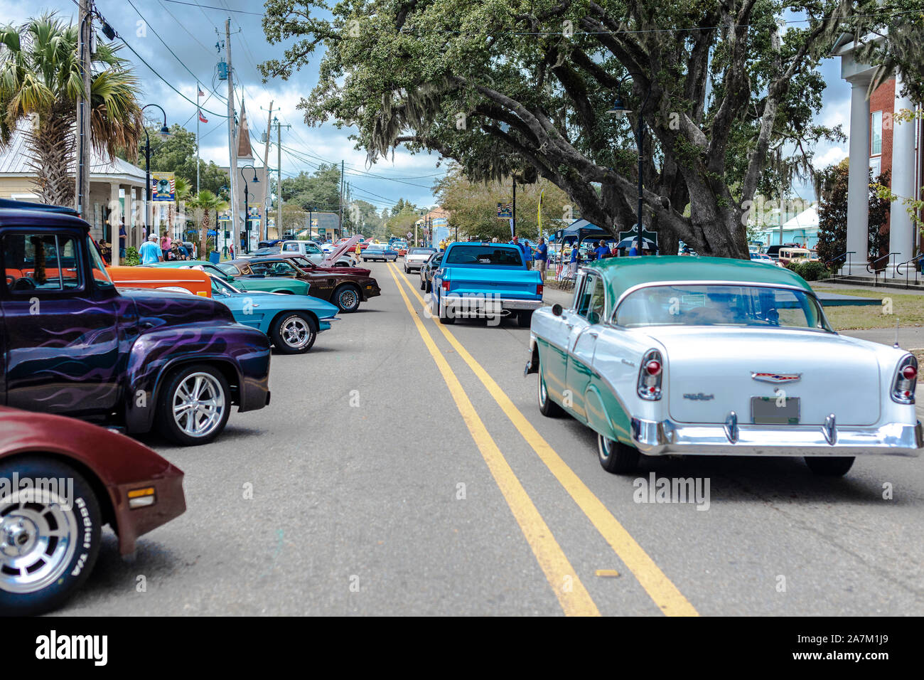 A Main Street Car Show with classic cars parked on the sides and vintage cars driving on the road. Stock Photo