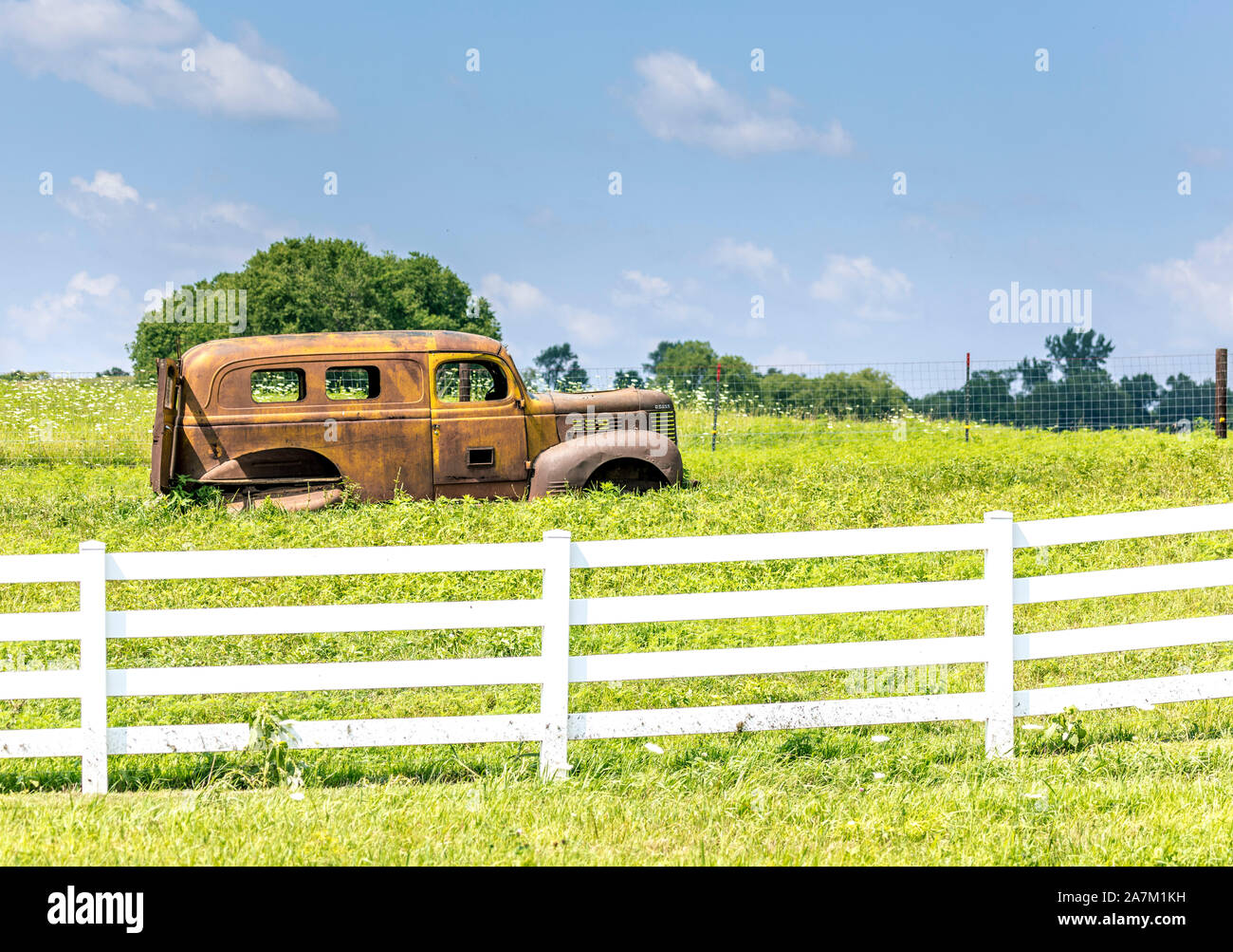 Abandoned rusty 1940 Dodge Panel Truck sitting in a field in the country behind a white fence. Stock Photo