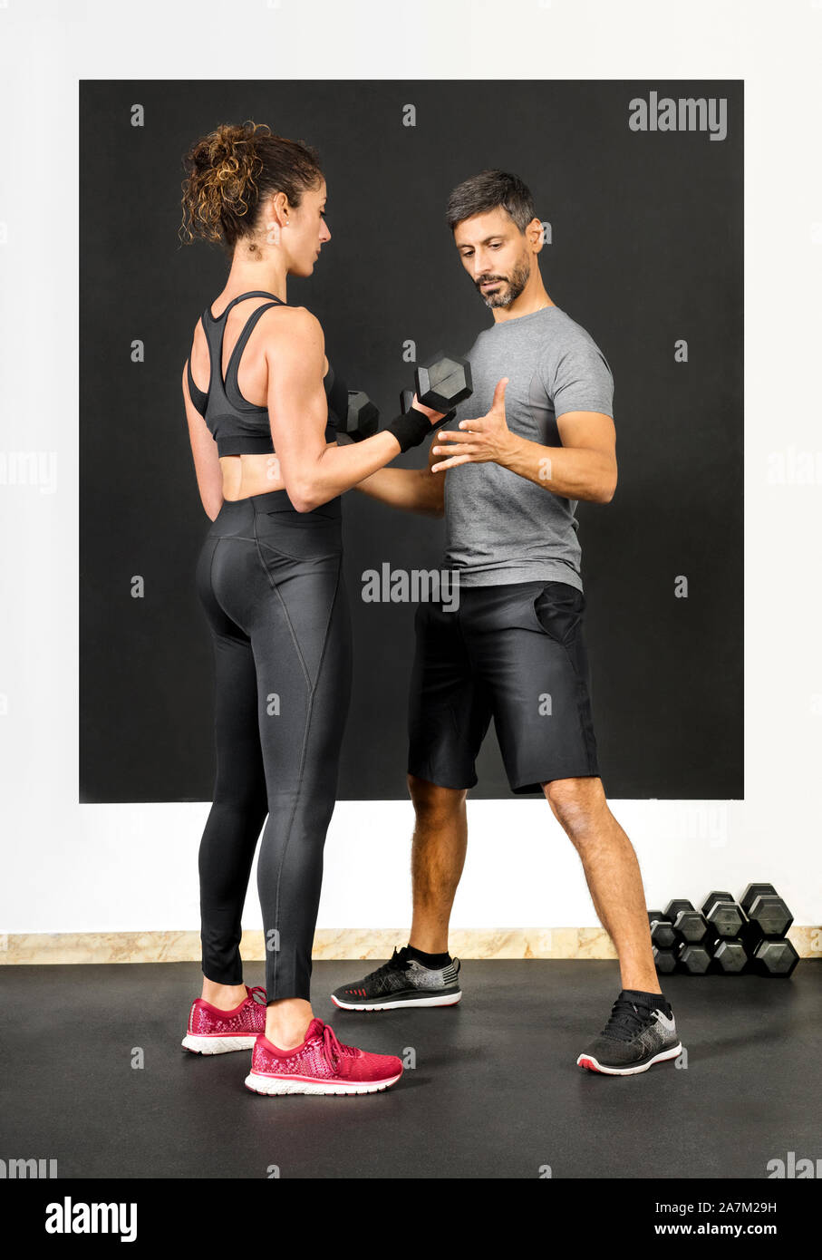 Male personal training assisting a woman with dumbbell weights in a gym as she works out strengthening her muscles in a health and fitness concept Stock Photo