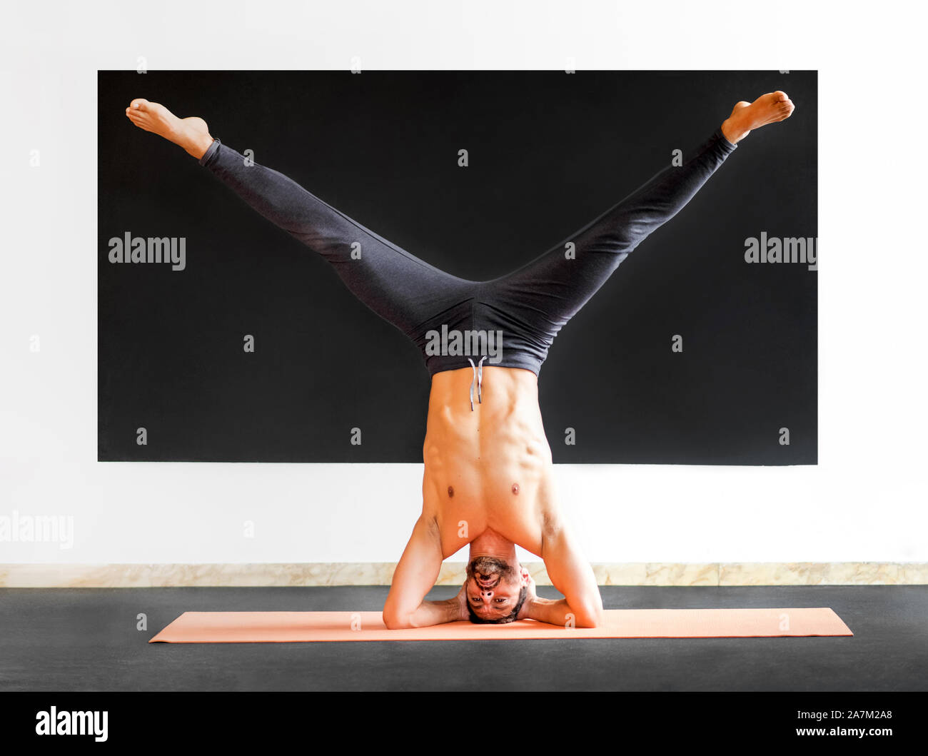 Athletic man doing a sirsasana heastand exercise while practising yoga in a gym in a health and fitness concept Stock Photo