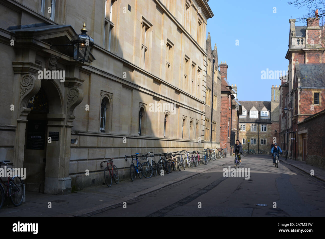Cyclists in Trinity Lane, with students bikes outside a college, University of Cambridge, Cambridge, Cambs., England Stock Photo