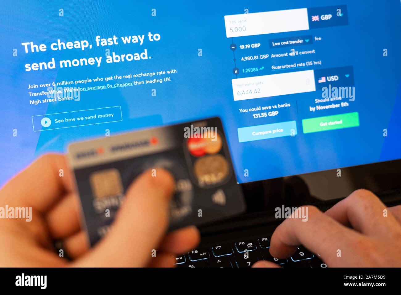 A hand holding a credit card and using TransferWise, a currency converter and money transfer website. Concept - online banking and fraud Stock Photo