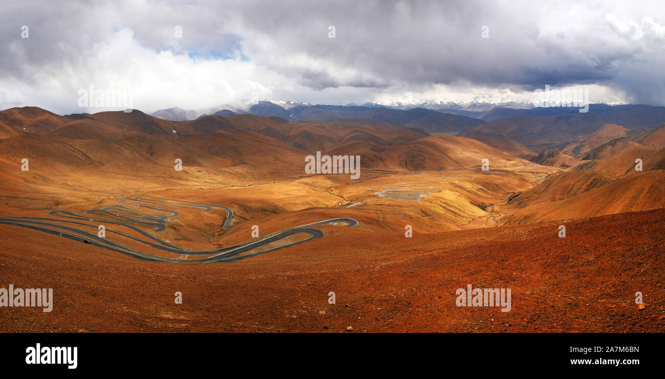 Panoramic view of highway stretching across the brown Himalaya Mountains, against a blue sky covered by white clouds. Stock Photo