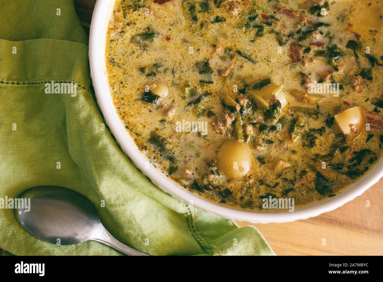 A large bowl of Zuppa Toscana soup shown with bright green napkin and spoon. Tuscan stew, Italian cuisine. Stock Photo