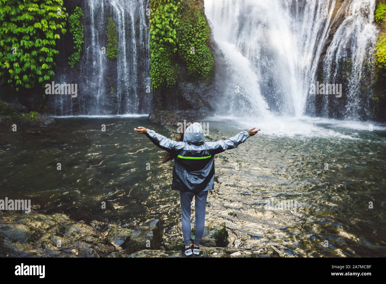 Young Happy Woman Enjoying Waterfall In Bali Wearing Grey Raincoat From Water Spray Travel In Indonesia Stock Photo Alamy