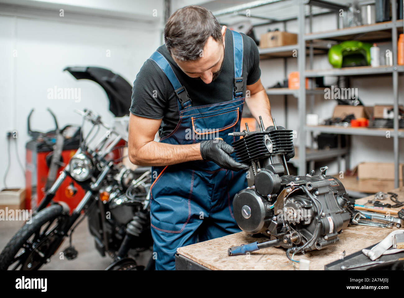 Workman in overalls disassembling motorcycle engine during a repairment at  the working table of the workshop Stock Photo - Alamy