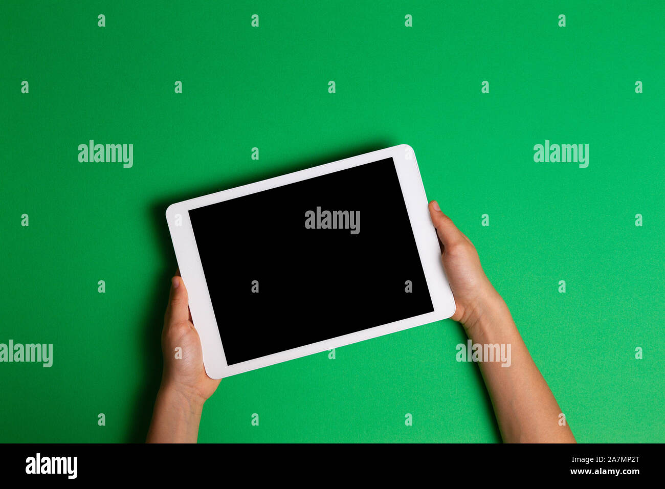 Kid hands holding white tablet computer on green background Stock Photo