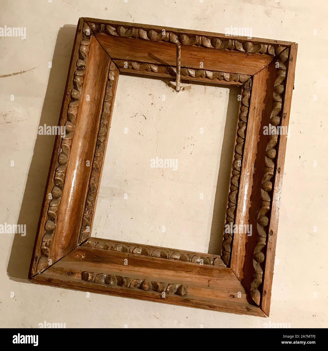Old wooden empty photo frame hanging on the wall nailed rusty steel nail. Vintage photo frame made of natural oak tree for fashion collage. Blank styl Stock Photo