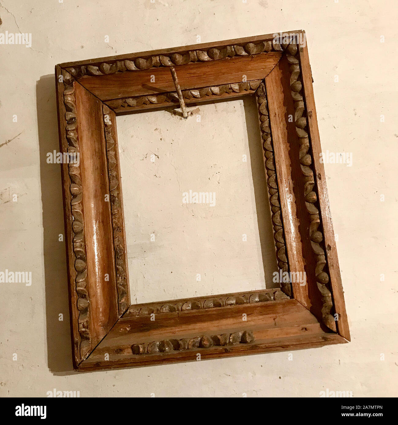 Old wooden empty photo frame hanging on the wall nailed rusty steel nail. Vintage photo frame made of natural oak tree for fashion collage. Blank styl Stock Photo
