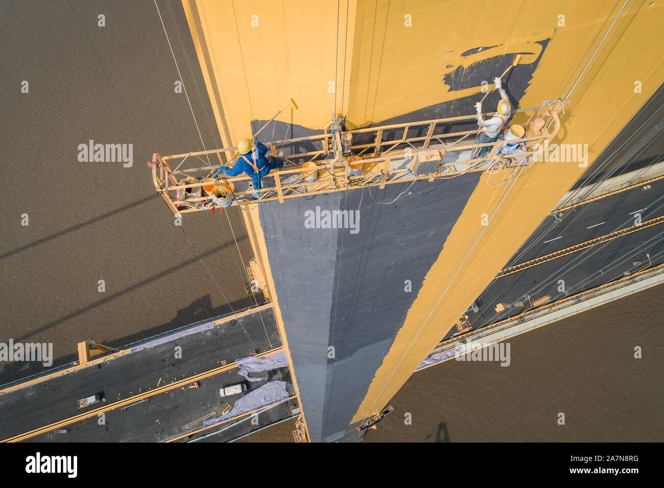 Chinese workers labor at the construction site, coating the pillars of the Yangsigang Bridge, the World's longest double-deck suspension bridge, acros Stock Photo