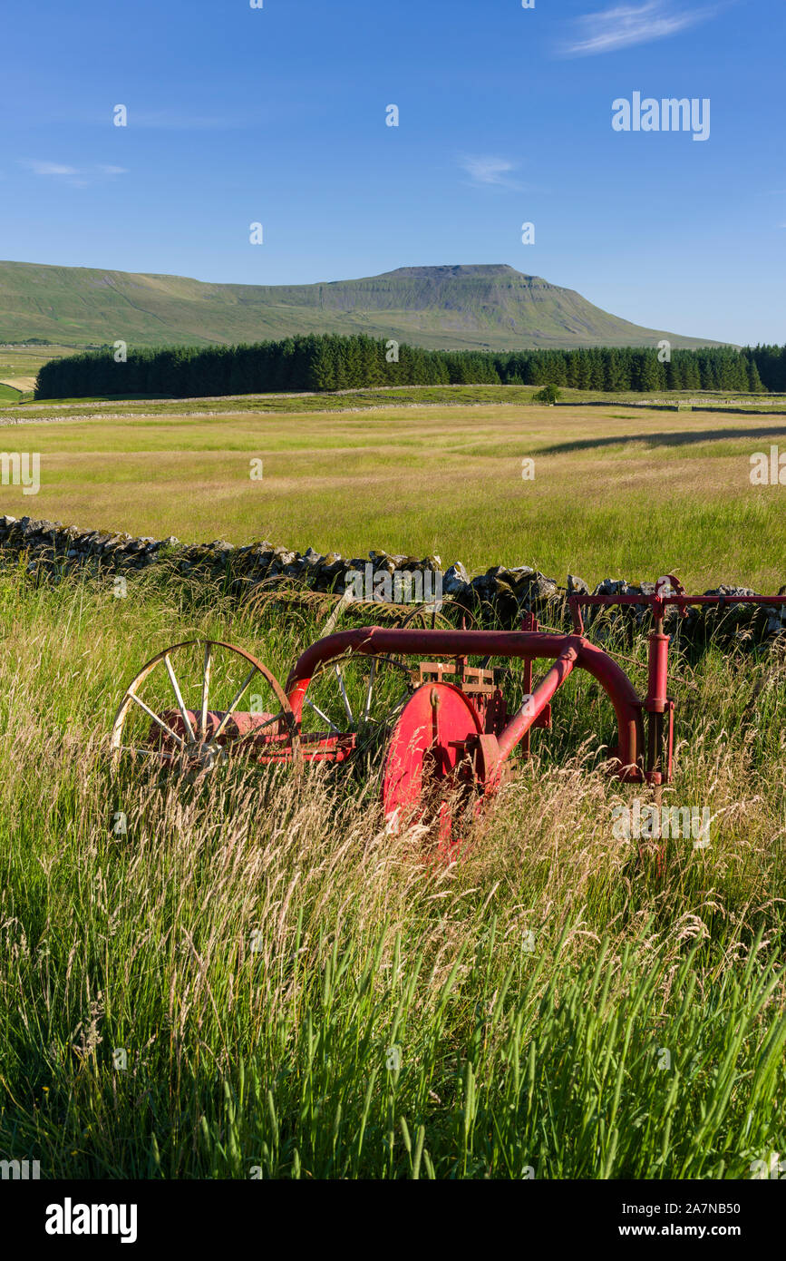 Farm machinery at the edge of a field in the Yorkshire Dales National Park with Ingleborough in the distance. Stock Photo