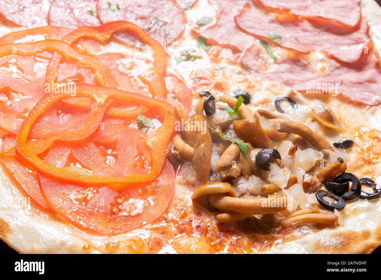Cheap pizza 4 seasons. With ham, pepperoni, mushrooms, and tomatoes. Stock Photo