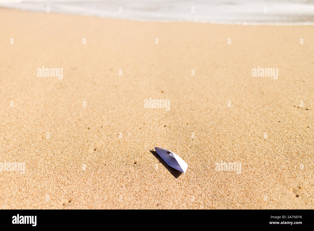Boat origami stranded on a beach, with foamy wave on the background Stock Photo