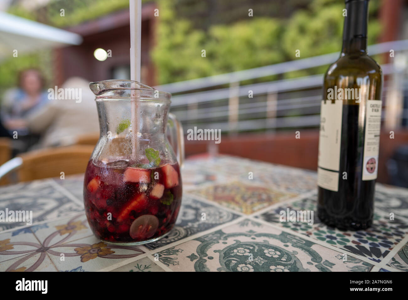 Pitcher of red sangria sitting next to red wine bottle on table at restaurant Stock Photo