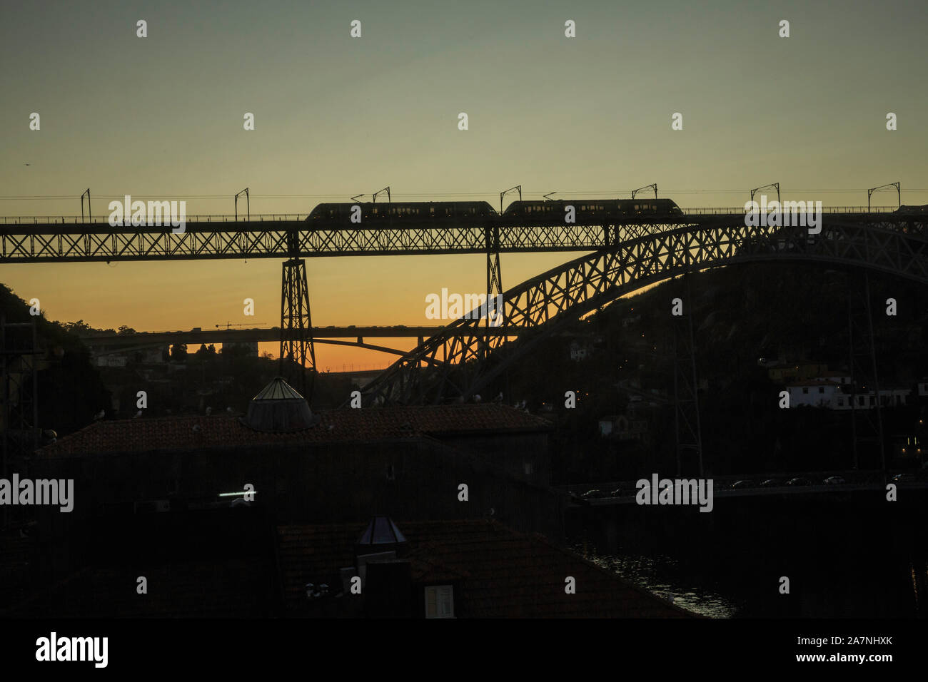 A new dawn creates striking silhouettes of bridges on which trains and cars move, the bridges spanning a river valley and river. Stock Photo