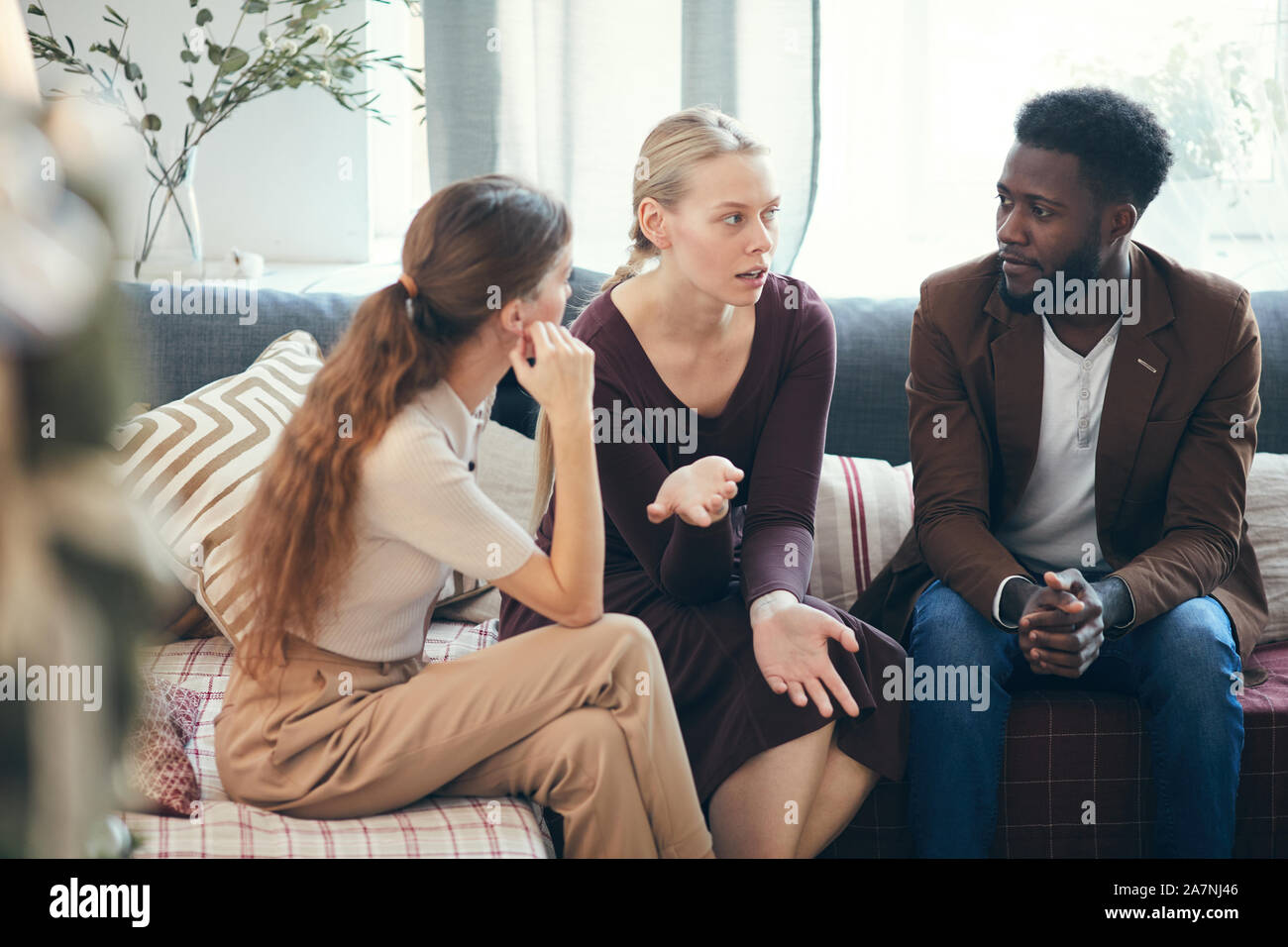 Group of modern young people talking to each other while sitting on cozy sofa and sharing stories, copy space Stock Photo