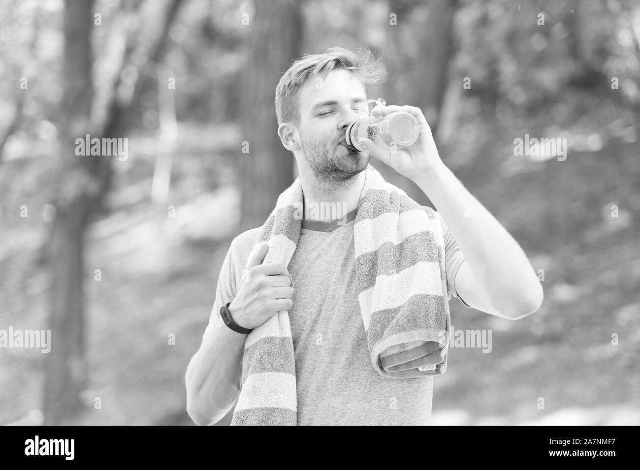 Water is indispensable for human health. Fit athlete having a drink from water bottle during training outdoor. Thirsty sportsman drinking pure water on hot summer day. Keeping body water balance. Stock Photo