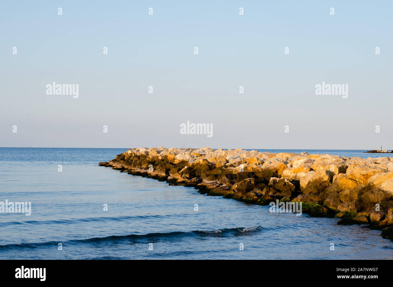 Stones  wave breaker  and  sea against  sunset  blue sky  during summer . Stock Photo
