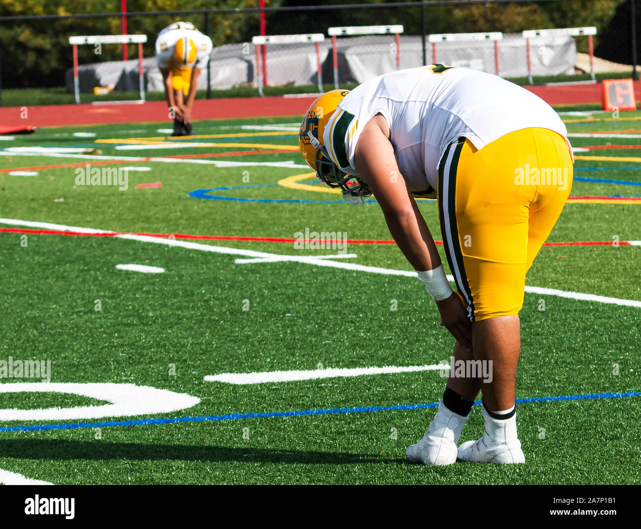 Two high school football players stretching on a green turf field before their game starts on a sunny Saturday afternoon. Stock Photo
