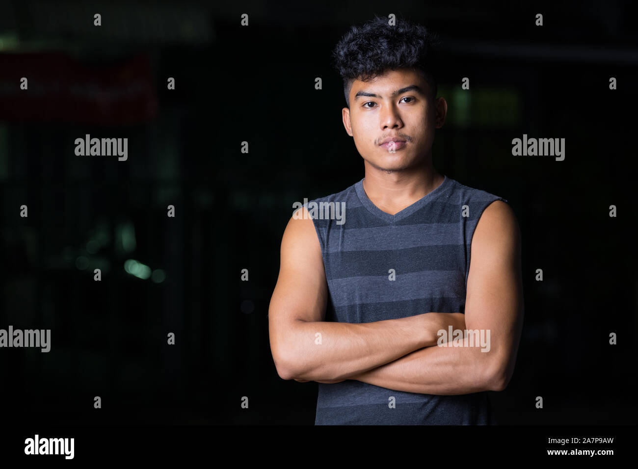 Young Asian man with arms crossed at night outdoors Stock Photo