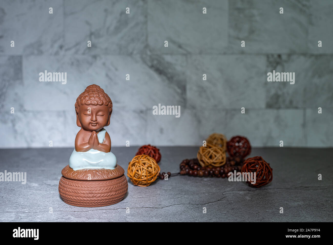 Monk sitting down praying statue home decoration ornament in spotlight casting shadow. Rattan cane balls, praying beads. Empty copy space for text. Ma Stock Photo