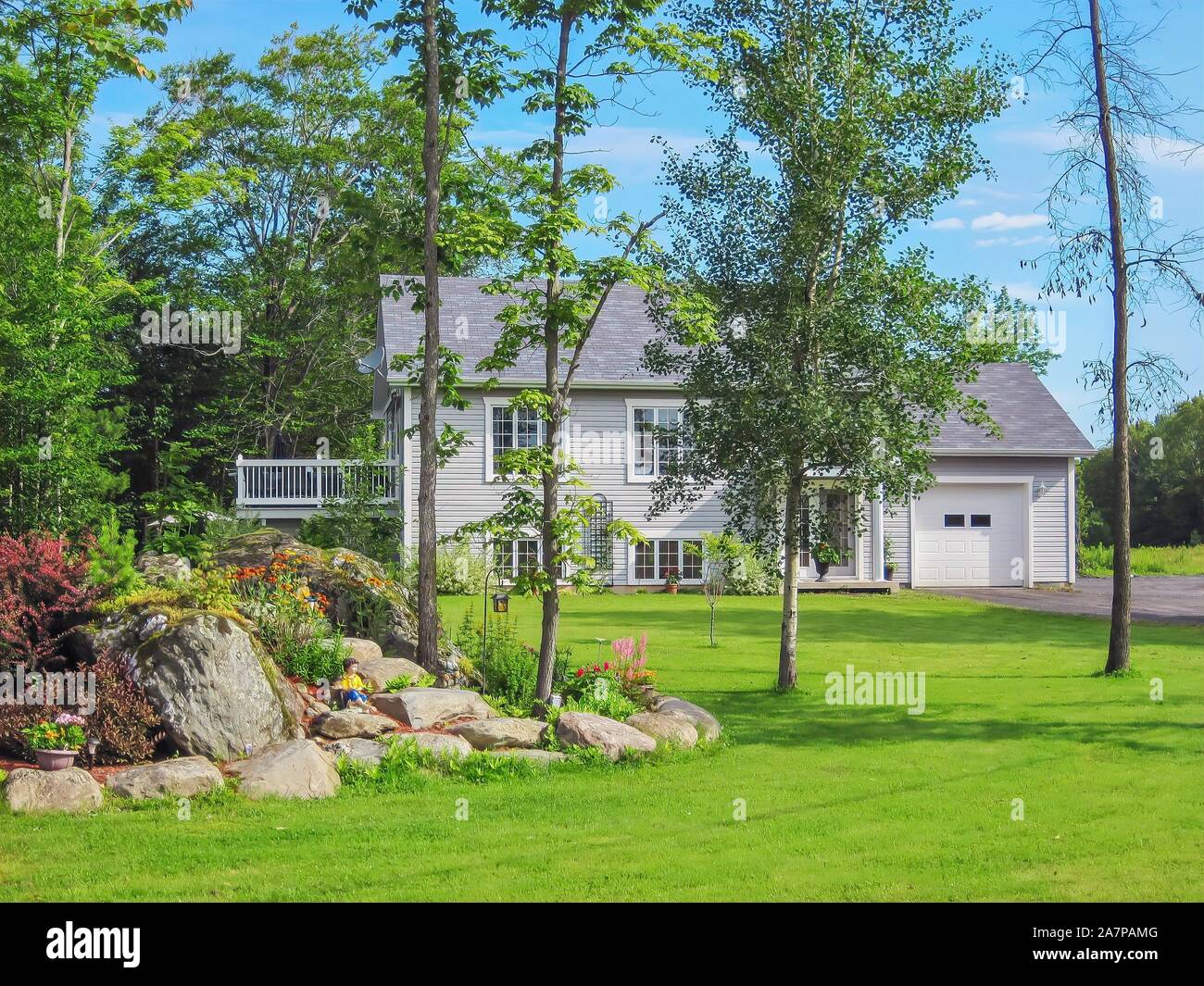 Street view of a picturesque country home with a large landscaped front yard in a forested rural area in the Eastern Townships of Quebec, Canada. Stock Photo
