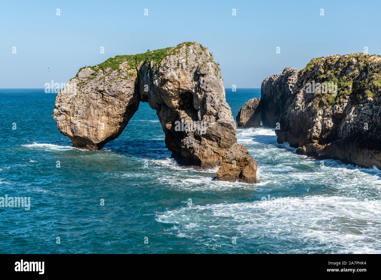 Scenic view of waves splashing against the rocky coast against blue sky. Castro de las Gaviotas, Fort of the Seagulls, and Beach of the Huelga, Llanes Stock Photo