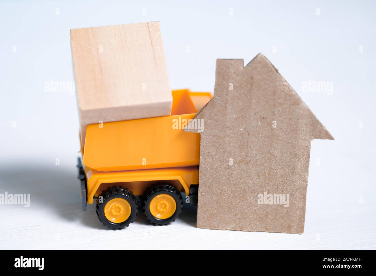 Orange toy truck with loaded wooden cube and cardboard cutout house on