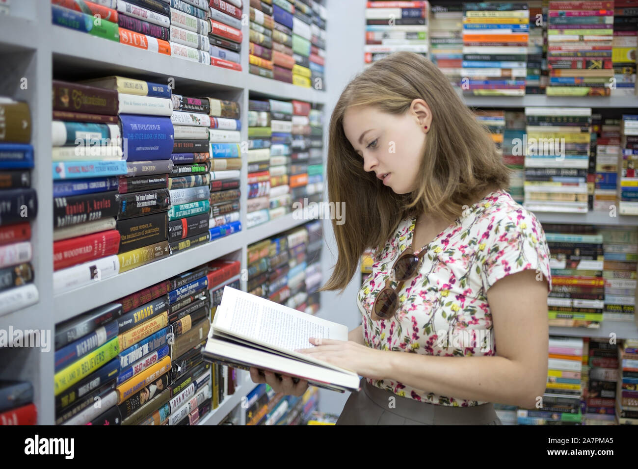 Manila, Philippines - June, 14, 2017: Smiling young caucasian woman girl choosing holding a book in library or bookstore Stock Photo