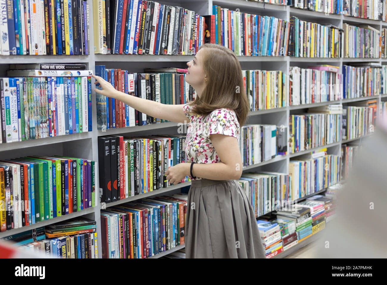 Manila, Philippines - June, 14, 2017: Smiling young caucasian woman girl choosing holding a book in library or bookstore Stock Photo
