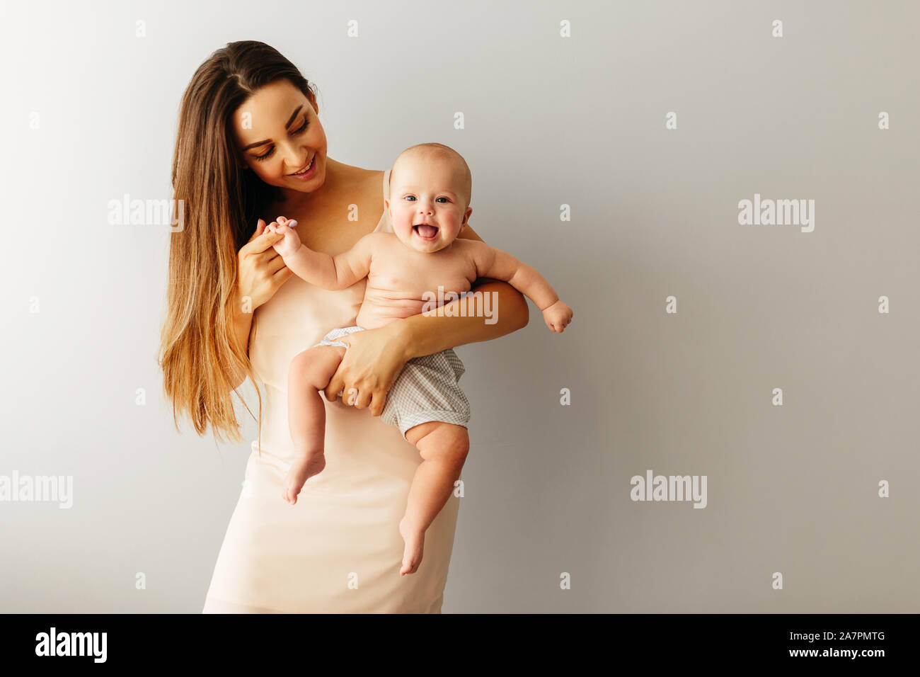beautiful happy mother holds her baby on a plain light background. Child is smiling Stock Photo