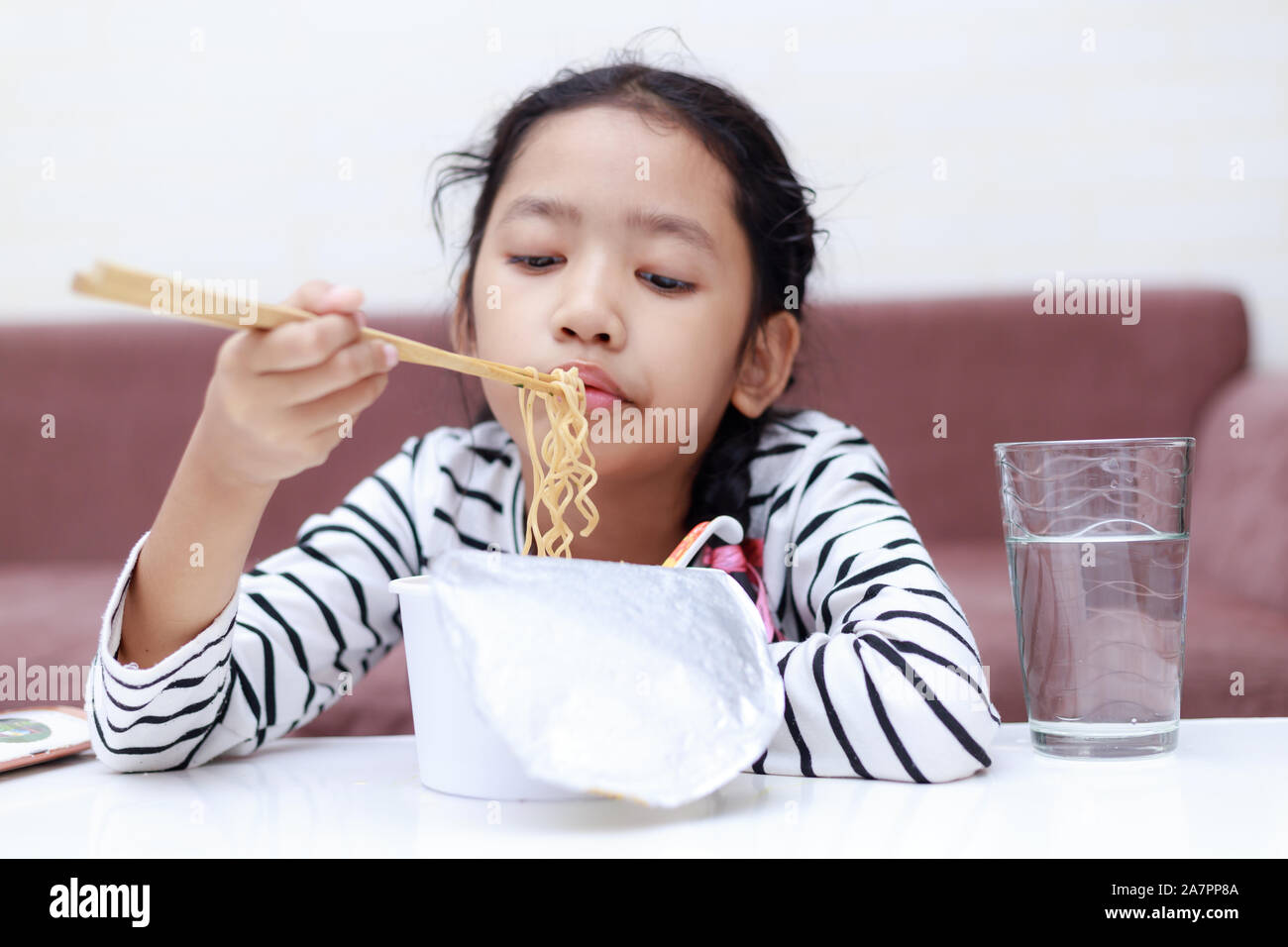 Little Asian girl sitting at white table to eating instant noodle and smile select focus shallow depth of filed Stock Photo