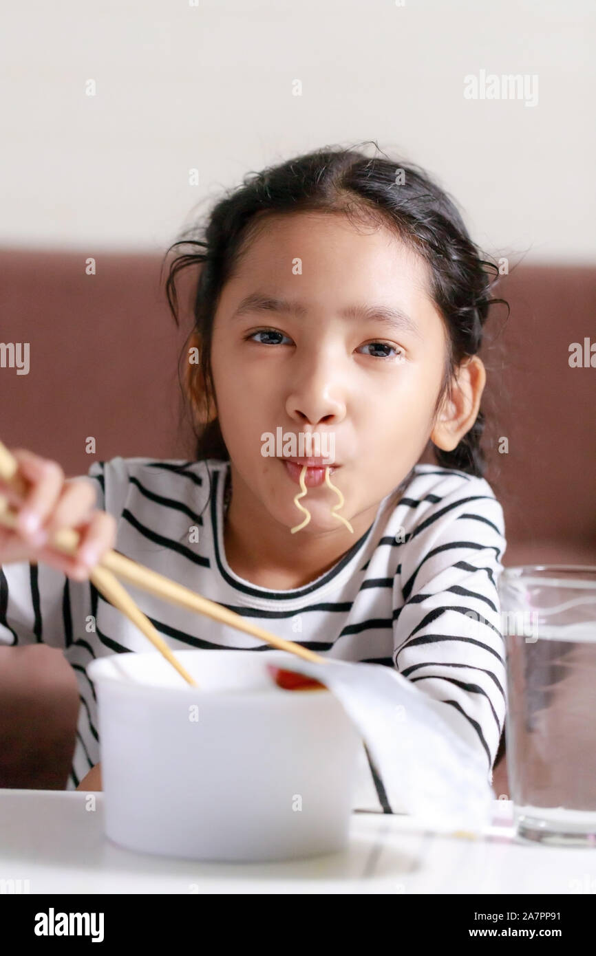 Happy little Asian girl sitting at white table to eating instant noodle  with deliciously select focus shallow depth of filed Stock Photo