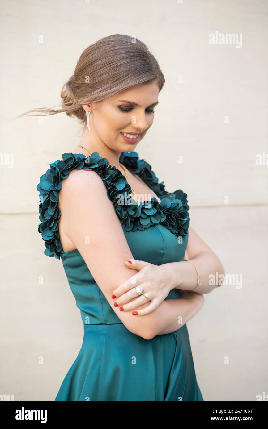 Happy woman wearing green evening gown arms folded looking down outdoors Stock Photo