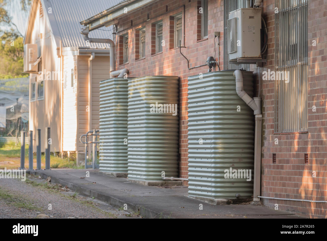Rain water tanks are against a brick wall at Bundeena Public School in Australia to support the local community garden Stock - Alamy