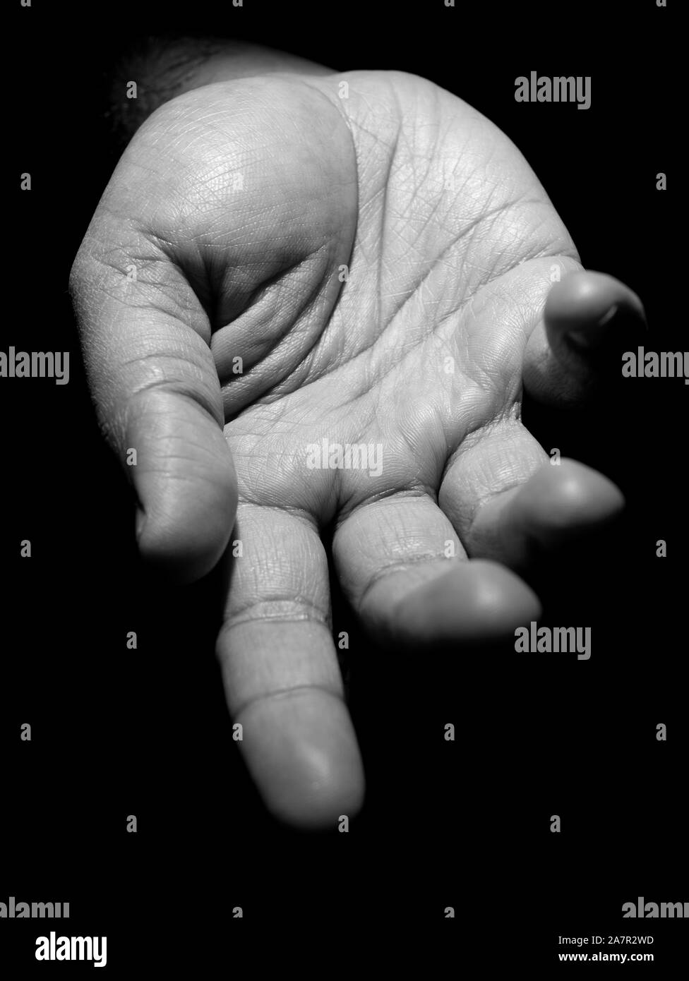 Black and white photo of a mans hand with fingers slightly apart asking for help in low key lighting Stock Photo