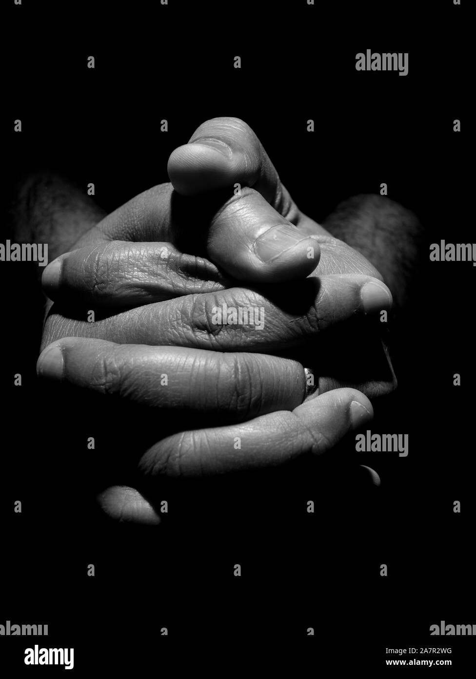 Black an white close up of a mans clasped hands in low key lighting Stock Photo