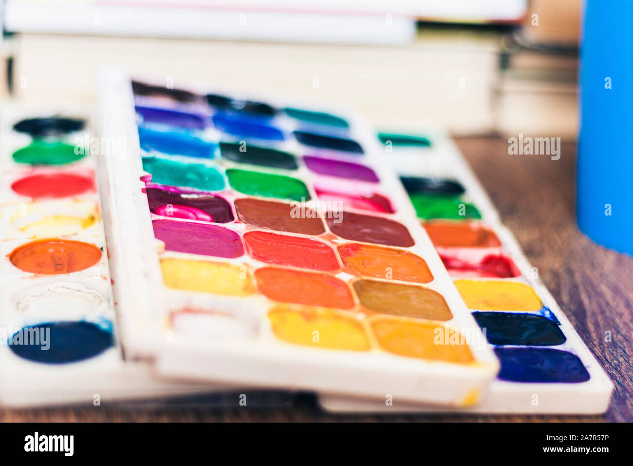 Watercolor paint, brushes well used on wooden table with stack of books