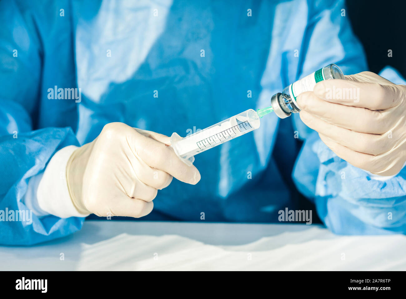 doctor in a blue surgical gown and mask holds in his hand a medical syringe and bottle with drugs for injection Stock Photo