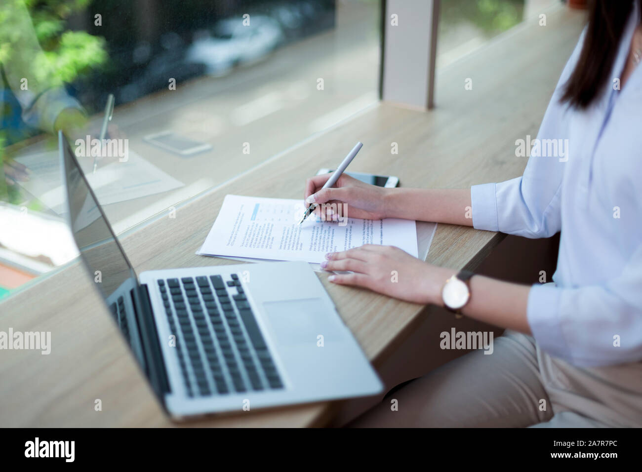Midsection shot of a businesswoman writing in a document while sitting at a desk with a laptop in an office Stock Photo