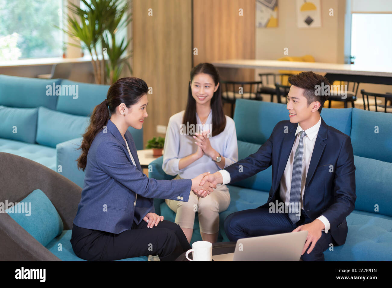 Photograph with three male and female businesspeople wearing businesswear with two of them shaking hands in an office Stock Photo