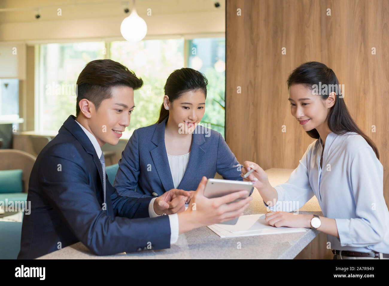 Group of three male and female young smiling businesspeople sitting together in an office and looking at a digital tablet held by one of them Stock Photo