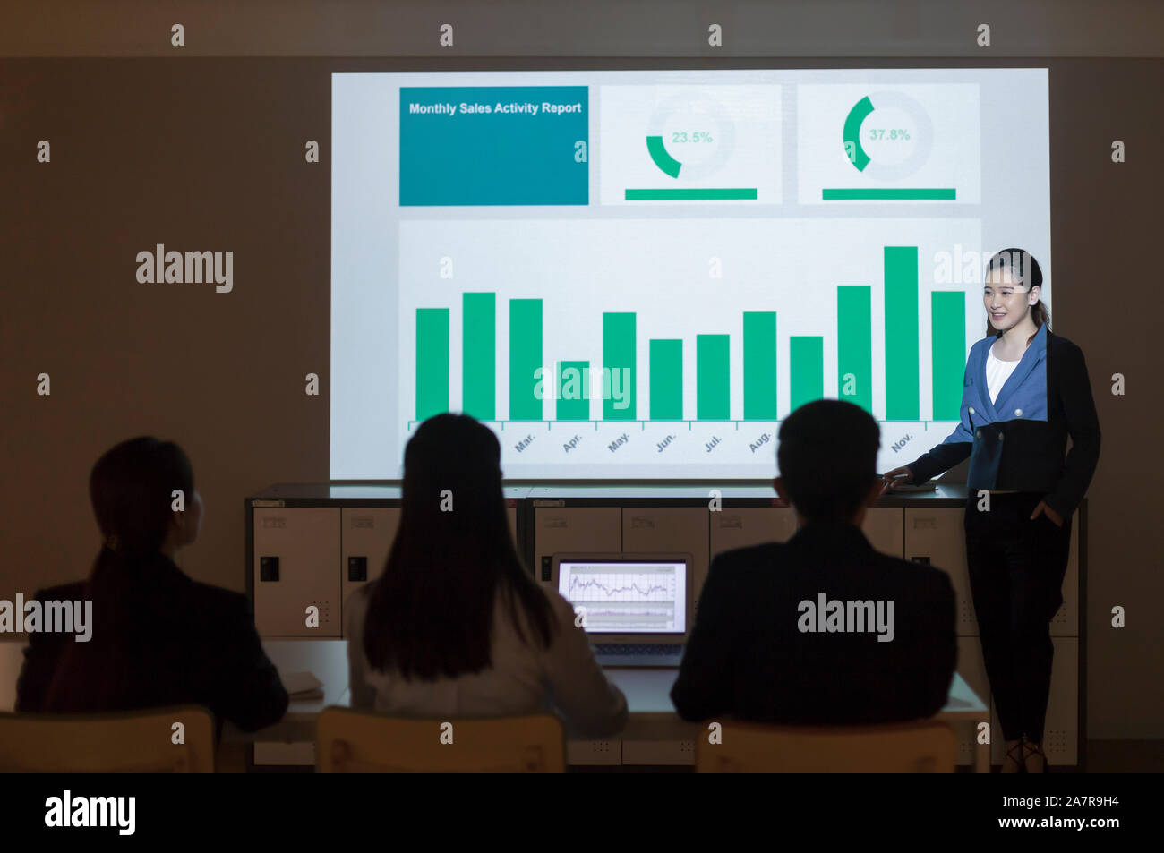 Photograph of a young businesswoman in businesswear giving a presentation with a chart on the screen behind her Stock Photo
