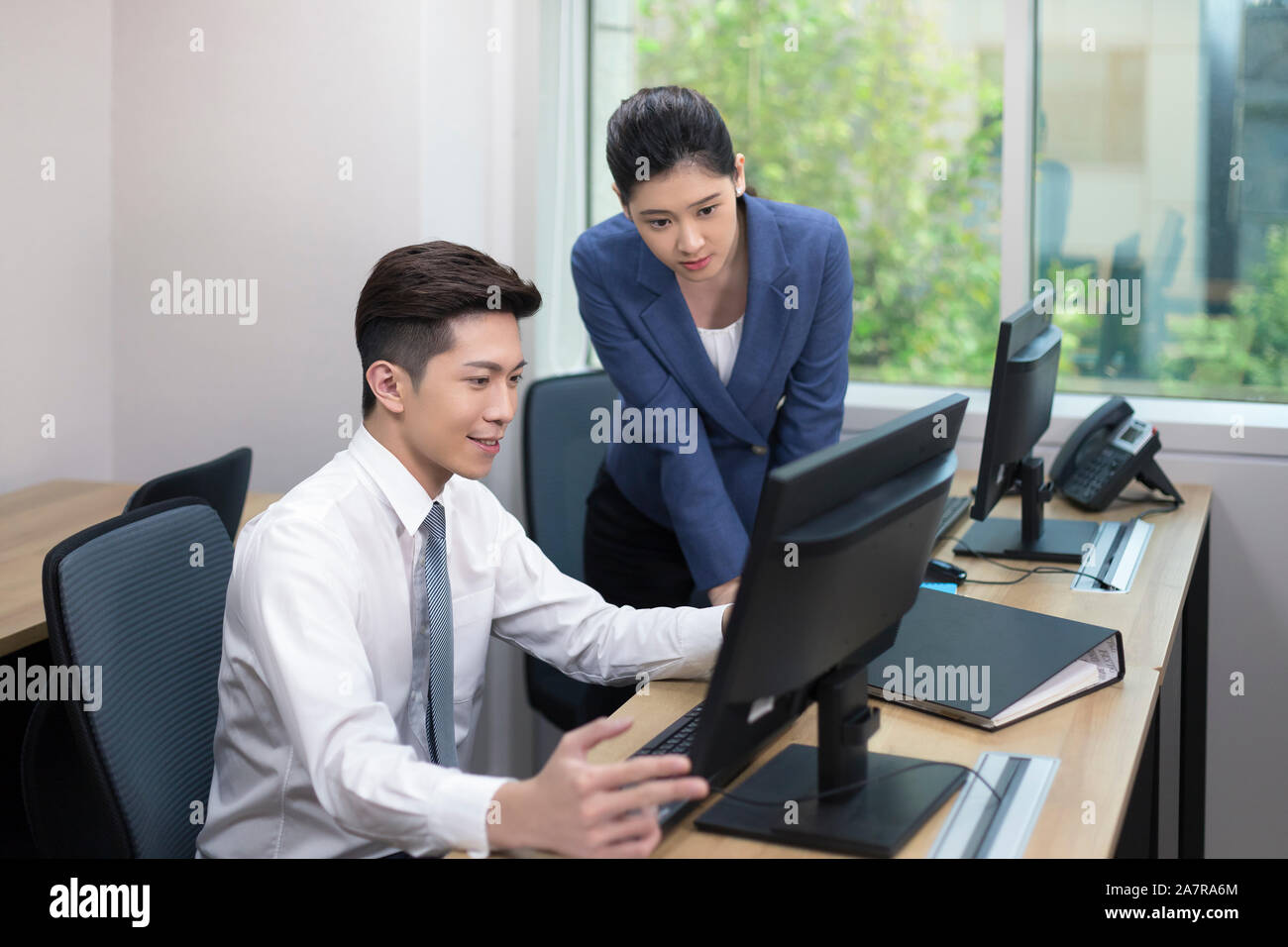 Two smiling young male and female businesspeople looking at a computer monitor of one of them while working together at a desk in an office Stock Photo