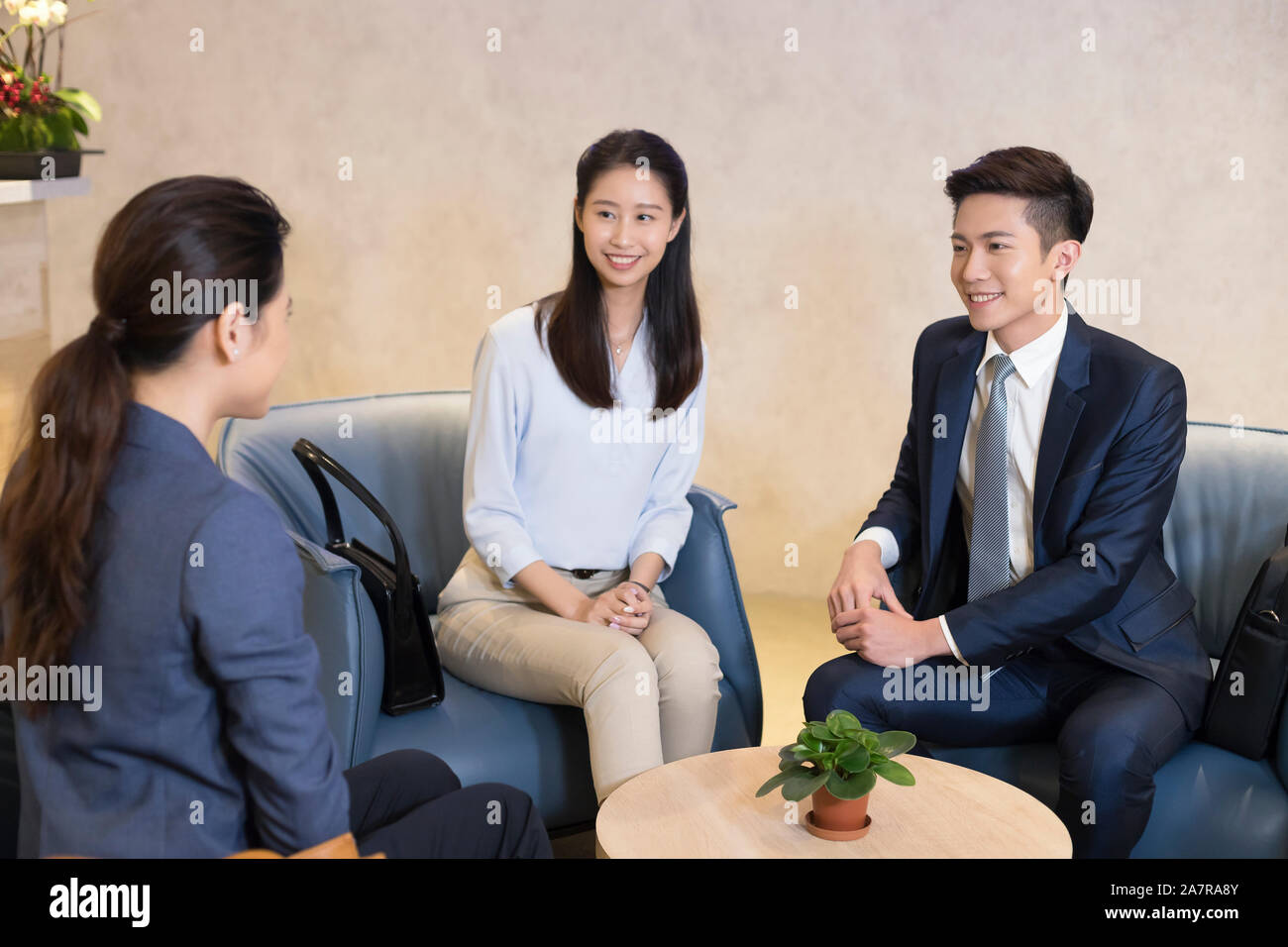 Photograph of a group of three smiling young male and female businesspeople talking together during a meeting Stock Photo