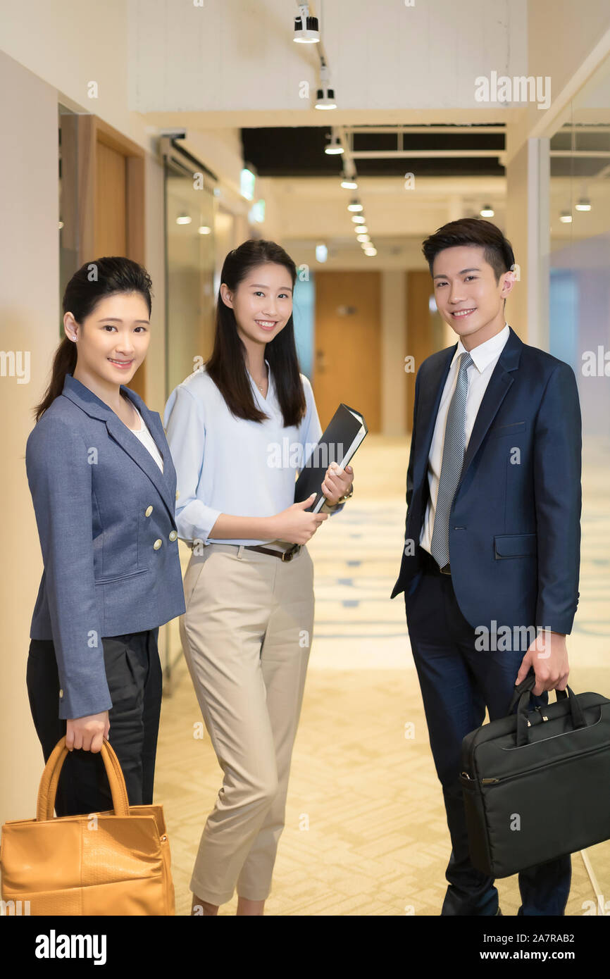 Portrait of three male and female young businesspeople standing in an office corridor, smiling at the camera Stock Photo