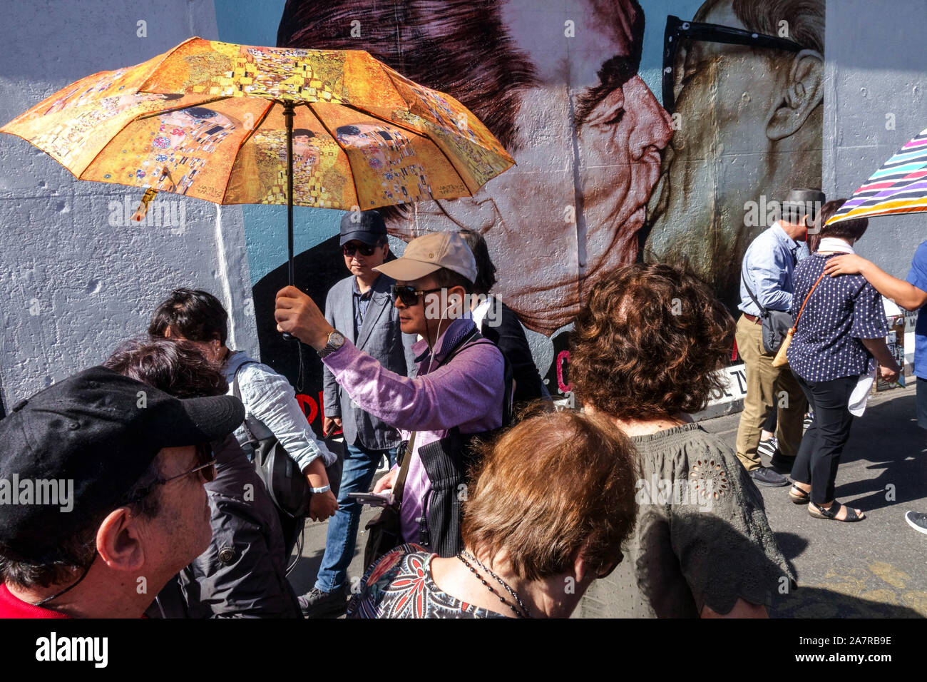 Berlin wall, Asian tourist group, a man with Gustav Klimt umbrella at East Side Gallery, Brezhnev Honecker kiss Germany Stock Photo
